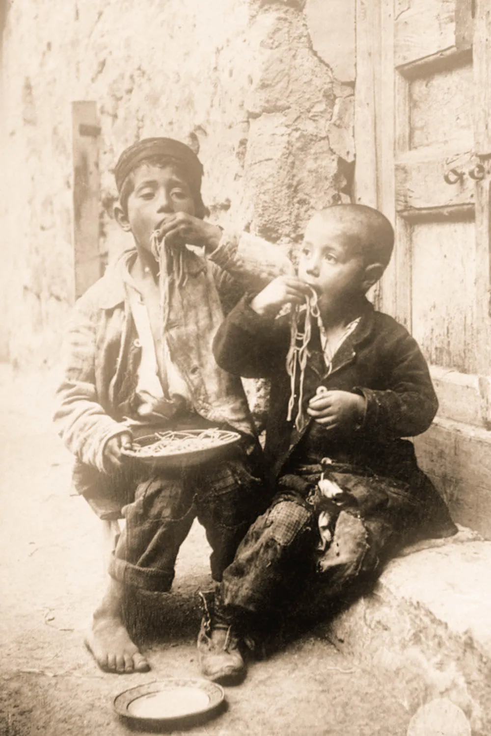 Niños comiendo espaguetis con las manos en imagen histórica en sepia