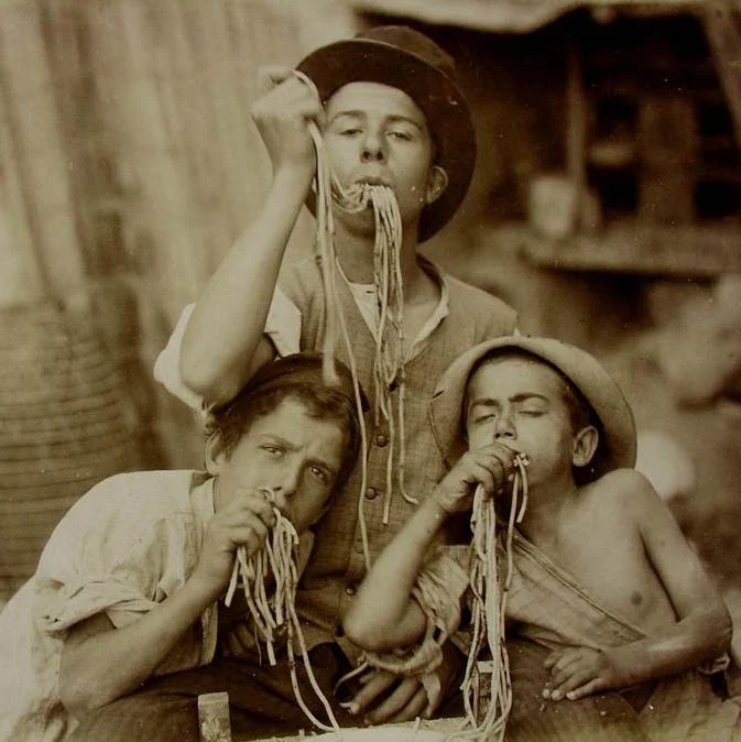 Tres niños comiendo espaguetis en una imagen vintage asociada a La Búfala de Alaró